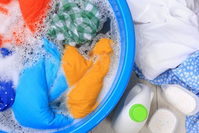 Basin with colorful clothes near bottle of detergent and powder on floor, flat lay Hand washing laundry