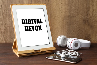 Tablet with phrase DIGITAL DETOX and different gadgets on wooden table