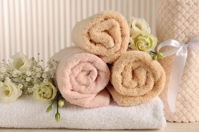 Photo of Soft towels, gypsophila and eustoma flowers on light wooden table, closeup