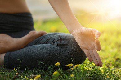 Woman meditating on green grass at sunrise, closeup view. Practicing yoga