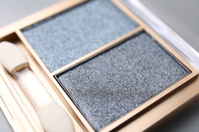 Photo of Beautiful eyeshadow palette with applicator on light gray background, closeup. Professional cosmetic product