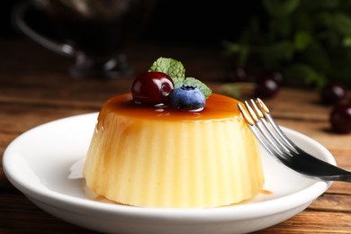 Photo of Plate of delicious caramel pudding with blueberry, cherry and mint served on wooden table, closeup