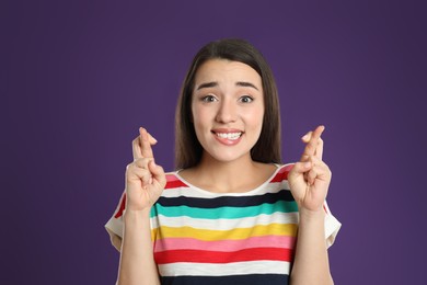 Woman with crossed fingers on purple background. Superstition concept
