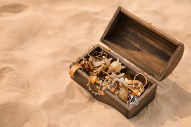 Photo of Open wooden chest with treasures on sand, space for text