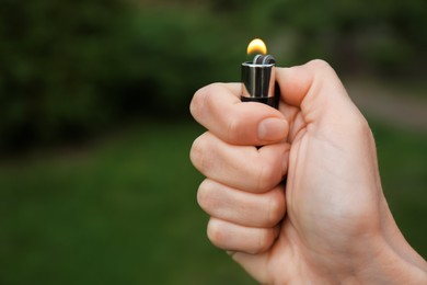 Man holding lighter with burning flame outdoors, closeup. Space for text