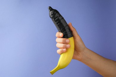 Woman holding banana in condom on light blue background, closeup and space for text. Safe sex concept