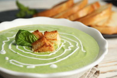 Bowl of delicious broccoli cream soup with croutons and basil on table, closeup