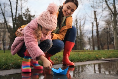 Little girl and her mother playing with paper boat near puddle in park