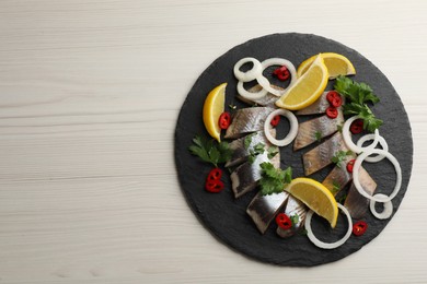 Slate plate with sliced salted herring fillet, parsley,  chili pepper, onion rings and lemon on light beige wooden table, top view. Space for text