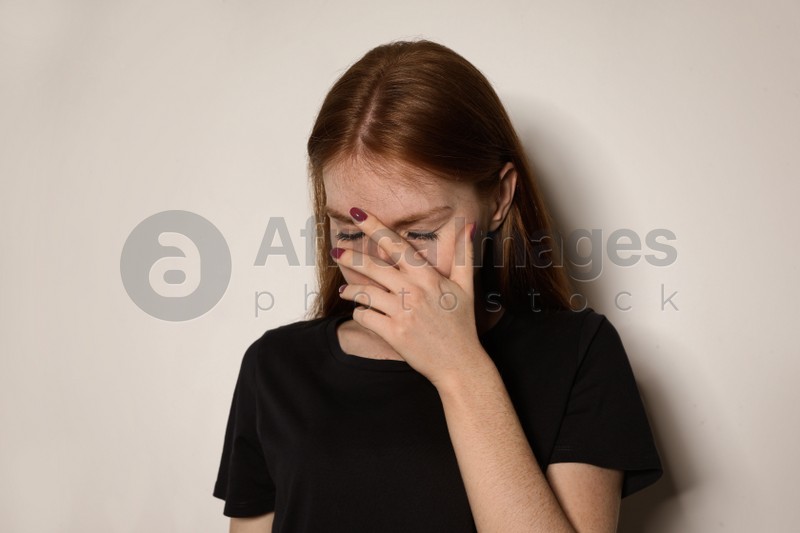 Young woman covering face against light background