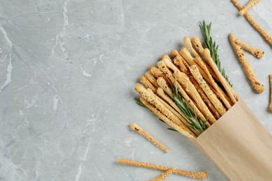Delicious grissini sticks and rosemary on grey marble table, flat lay. Space for text
