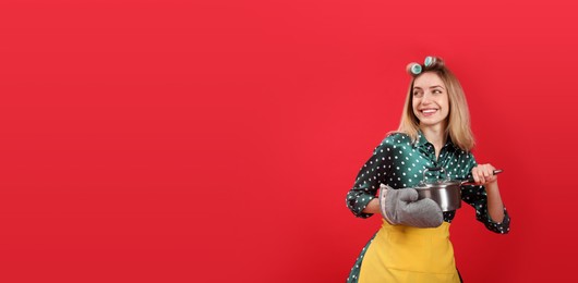 Young housewife with saucepan on red background. Space for text