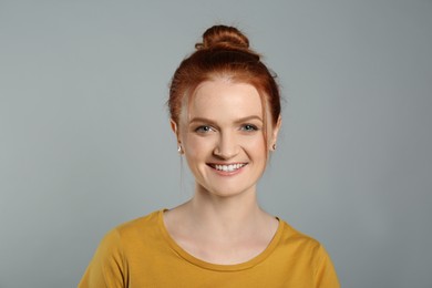 Candid portrait of happy red haired woman with charming smile on grey background
