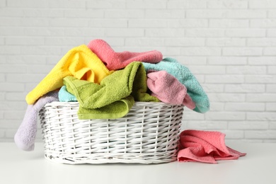 Wicker basket with towels on table near white brick wall