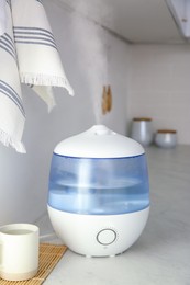 Photo of Modern air humidifier, cup and bamboo mat on counter in kitchen