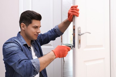 Handyman with screw gun repairing door lock indoors