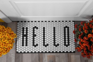 Stylish door mat with word Hello and beautiful flowers, flat lay