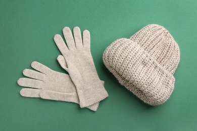 Woolen gloves and hat on green background, flat lay