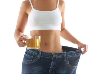 Young woman in old big jeans with cup of tea showing her diet results on white background, closeup