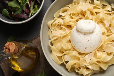 Delicious pasta with burrata cheese served on black table, flat lay
