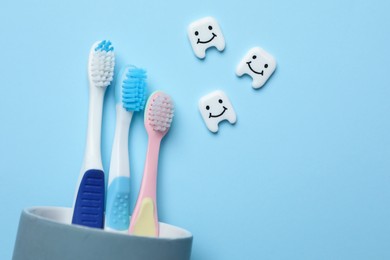 Plastic teeth with cute faces and toothbrushes on light blue background, flat lay. Space for text