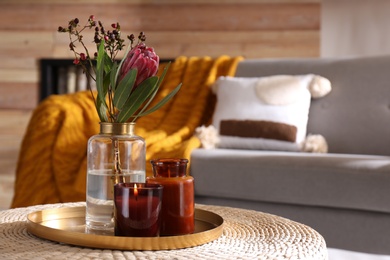 Photo of Vase with beautiful protea flower and candles on wicker stand indoors, space for text. Interior elements