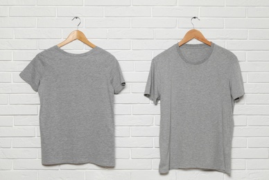 Hangers with blank t-shirts on white brick wall. Mock up for design