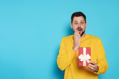 Photo of Surprised man with gift box on light blue background, space for text