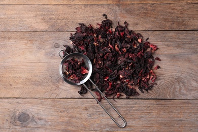 Dry hibiscus tea and sieve on wooden table, flat lay