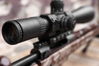 Closeup view of modern powerful sniper rifle with telescopic sight on blurred background