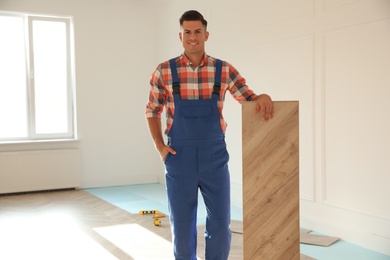 Professional worker with wooden board indoors. Installing of parquet flooring