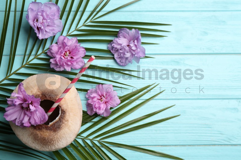 Photo of Young peeled coconut with straw, tropical leaves and flowers on light blue wooden table, flat lay. Space for text