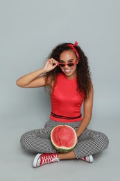 Beautiful young African American woman with half of watermelon on grey background