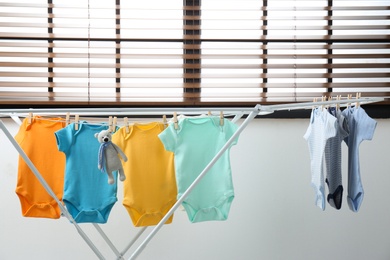 Different cute baby onesies hanging on clothes line indoors. Laundry day