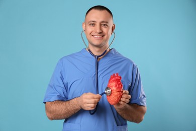 Photo of Doctor with stethoscope and model of heart on light blue background. Cardiology concept