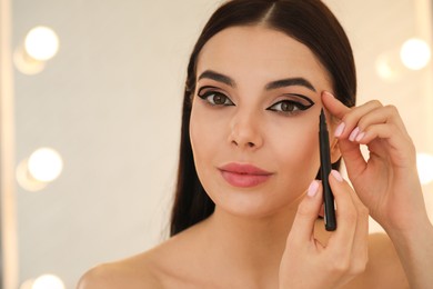 Photo of Beautiful young woman applying black eyeliner indoors. Space for text