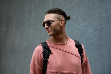 Handsome young man in stylish sunglasses and backpack near grey wall