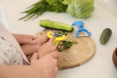 Mother teaching daughter to peel vegetable at kitchen counter, closeup