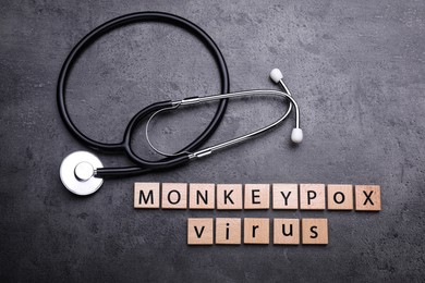 Photo of Words Monkeypox Virus made of wooden squares and stethoscope on grey table, flat lay