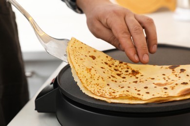 Photo of Man cooking delicious crepe on electric pancake maker at table, closeup