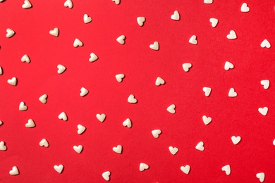 White heart shaped sprinkles on red background, flat lay