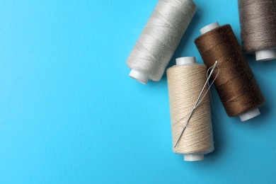 Different colorful sewing threads with needle on light blue background, flat lay. Space for text