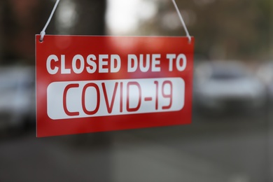 Red sign with words "Closed Due To Covid-19" hanging on glass door