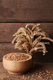 Wheat grains in bowl and spikes on wooden table