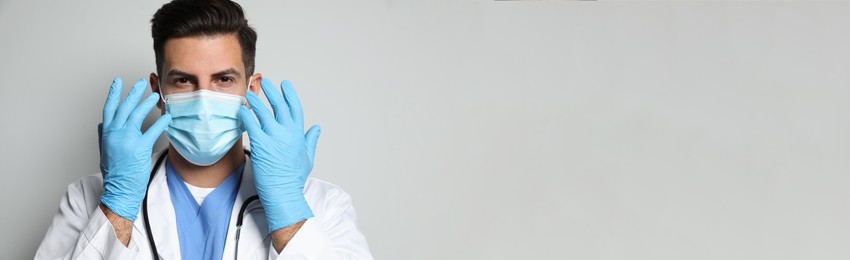 Doctor in protective mask and medical gloves against light grey background. Banner design with space for text 