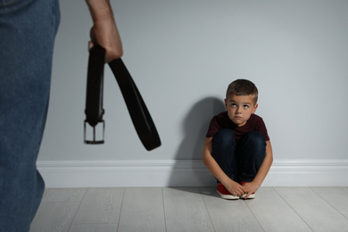 Photo of Man threatening his son with belt indoors. Domestic violence concept