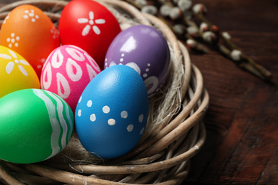 Colorful Easter eggs in decorative nest on wooden background, closeup