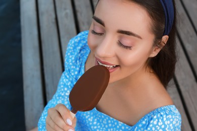 Beautiful young woman eating ice cream glazed in chocolate on pier, closeup