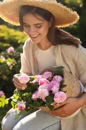 Young woman holding wicker basket with beautiful tea roses in garden, closeup