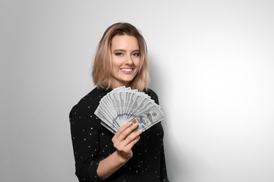 Portrait of young woman with money fan on light background